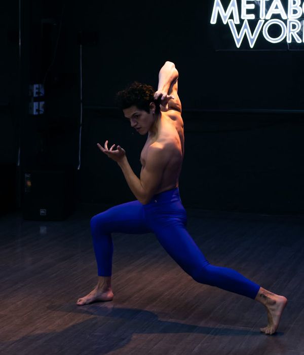 Man performing a controlled strength pose in a minimalist dark studio.